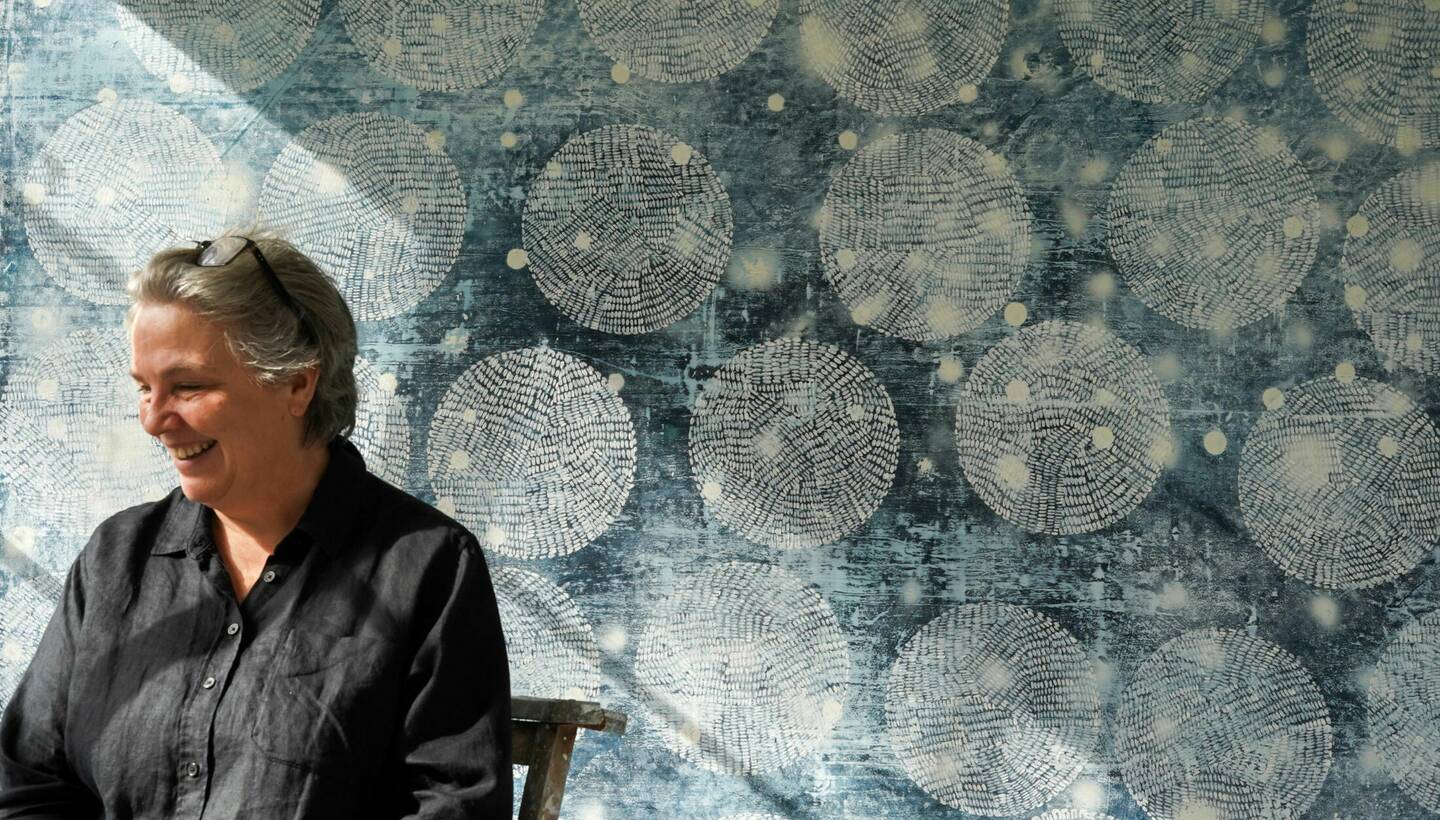 Photograph of Helen Booth seated in front of her painting.